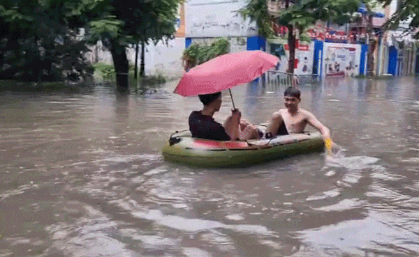 Mưa to, nước ngập sâu, nam thanh niên dùng thuyền phao giữa đường phố Hà Nội
